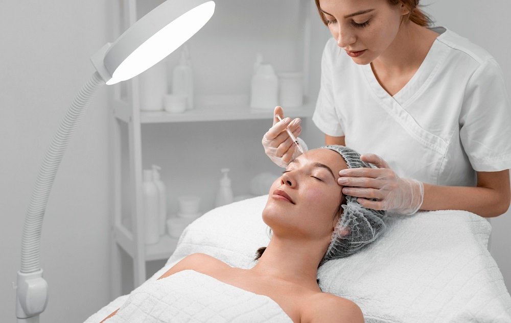 A medical professional in gloves injects a substance into a woman's forehead during a skin treatment procedure.