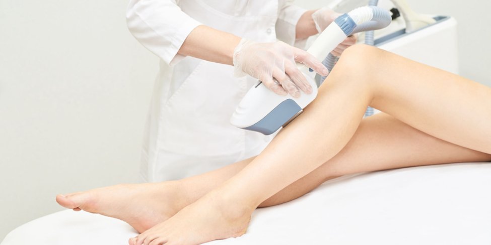A medical professional with gloved hands uses a laser device to perform hair removal on a person's legs.