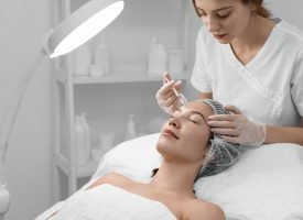 A medical professional in gloves injects a substance into a woman's forehead during a skin treatment procedure.
