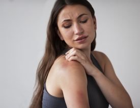 Skin Irritation or Rash A woman touches her shoulder, which has a visible red rash or irritation.